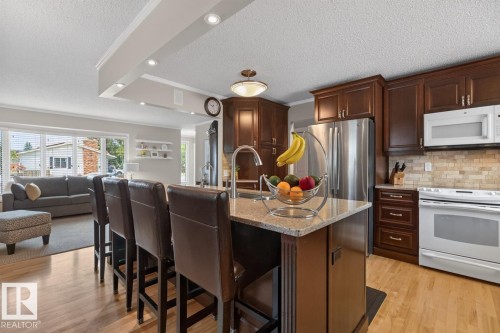 Kitchen featuring a spacious island with granite-style countertop, stainless steel refrigerator, white range, and wood cabinetry - 27 Milford Crescent, Sherwood Park, AB - Indoor Photo Showing Kitchen
