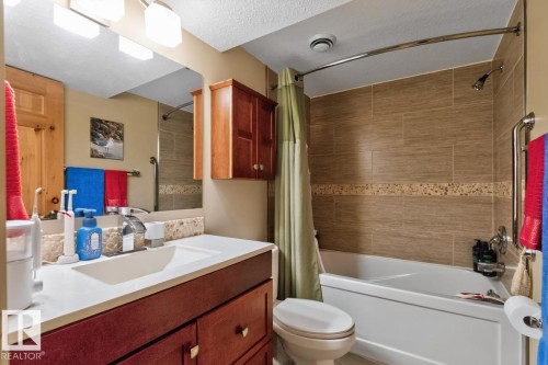 Spa-inspired bathroom featuring a wood-finish vanity with dual-sink configuration, ceramic tile surround in warm earth tones with decorative tile band detail, and an integrated bathtub-shower combination with coordinating tile work - 27 Milford Crescent, Sherwood Park, AB - Indoor Photo Showing Bathroom