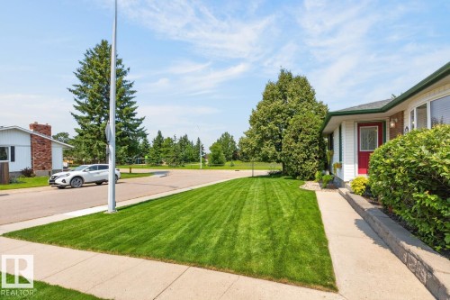 Pristine front grounds featuring manicured lawn with professional striping, mature landscaping, concrete driveway, and brick exterior with red accent door - 27 Milford Crescent, Sherwood Park, AB - Outdoor