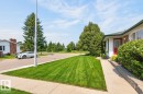 Pristine front grounds featuring manicured lawn with professional striping, mature landscaping, concrete driveway, and brick exterior with red accent door - 27 Milford Crescent, Sherwood Park, AB  - Outdoor 