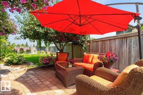 Brick paver patio featuring a perimeter garden bed, mature trees, manicured lawn, and wood fencing - 27 Milford Crescent, Sherwood Park, AB - Outdoor With Deck Patio Veranda