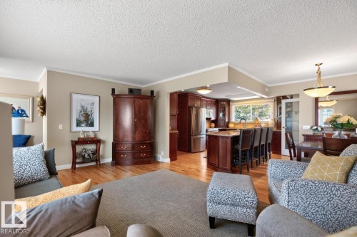 Open-concept living area showcasing rich hardwood flooring, custom cherry wood cabinetry and built-in bar seating, recessed ceiling detail with pendant lighting, and elegant upholstered seating - 27 Milford Crescent, Sherwood Park, AB - Indoor Photo Showing Living Room