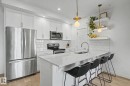 Modern kitchen featuring a large island with a light-toned countertop, stainless steel appliances, white subway tile backsplash, white cabinetry, and wood-finish flooring - #435 1008 Rosenthal Bv Nw, Edmonton, AB  - Indoor Photo Showing Kitchen With Stainless Steel Kitchen With Double Sink With Upgraded Kitchen 