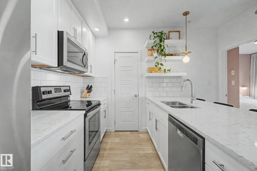 Well-appointed kitchen featuring white cabinetry, light-toned countertops, stainless steel appliances, a subway tile backsplash, and light wood-finish flooring - #435 1008 Rosenthal Bv Nw, Edmonton, AB - Indoor Photo Showing Kitchen With Stainless Steel Kitchen With Double Sink With Upgraded Kitchen