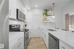 Well-appointed kitchen featuring white cabinetry, light-toned countertops, stainless steel appliances, a subway tile backsplash, and light wood-finish flooring - 