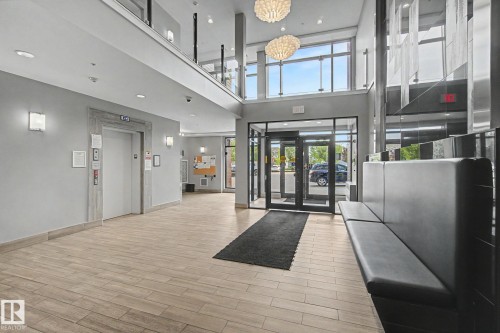 Modern lobby featuring wood-finish flooring, a built-in bench, dual decorative chandeliers, and a glass-paneled entry - #435 1008 Rosenthal Bv Nw, Edmonton, AB - Indoor Photo Showing Other Room