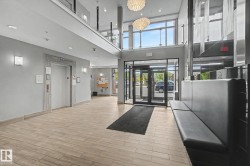 Modern lobby featuring wood-finish flooring, a built-in bench, dual decorative chandeliers, and a glass-paneled entry - 