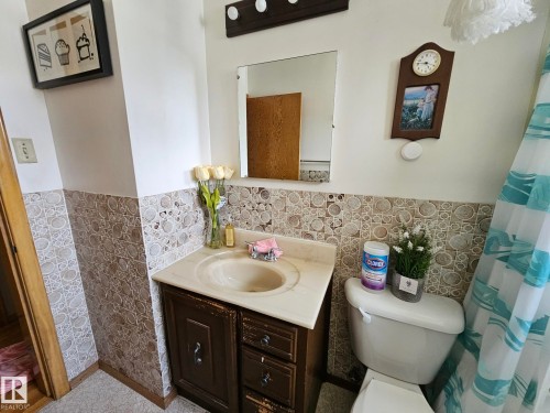 Bathroom featuring patterned wall tile, a single vanity with an integrated sink, and a toilet - 13103 63 Street Nw, Edmonton, AB - Indoor Photo Showing Bathroom