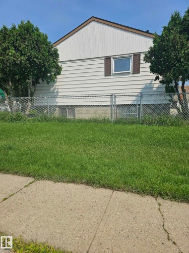White siding exterior featuring a brown roofline trim, a single window with brown shutters, and mature trees - 13103 63 Street Nw, Edmonton, AB - Outdoor