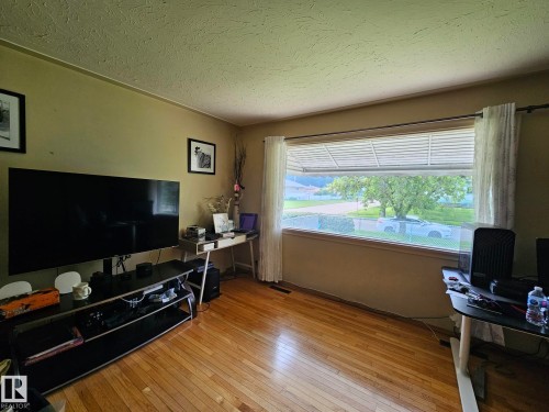 Living room featuring wood-finish flooring, a large picture window with horizontal blinds, and neutral wall tones - 13103 63 Street Nw, Edmonton, AB - Indoor