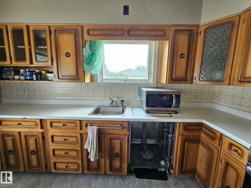 Kitchen featuring wood cabinetry with glass-front accents, laminate countertops, a stainless steel sink, and patterned tile backsplash - 13103 63 Street Nw, Edmonton, AB - Indoor Photo Showing Kitchen