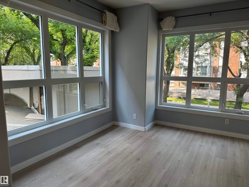 Bright room featuring extensive multi-pane windows, light wood-finish flooring, and painted walls with white trim - #203 11103 84 Av Nw, Edmonton, AB - Indoor Photo Showing Other Room