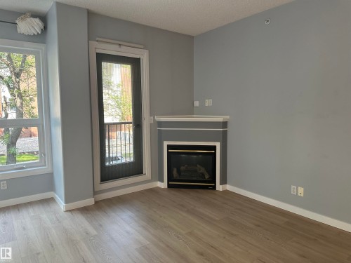 Living area featuring a corner fireplace with a white mantel, light wood-finish flooring, and light grey painted walls - #203 11103 84 Av Nw, Edmonton, AB - Indoor Photo Showing Living Room With Fireplace