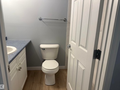 Bathroom featuring a white toilet, light wood-finish flooring, and a vanity with a white cabinet and speckled blue countertop - #203 11103 84 Av Nw, Edmonton, AB - Indoor Photo Showing Bathroom
