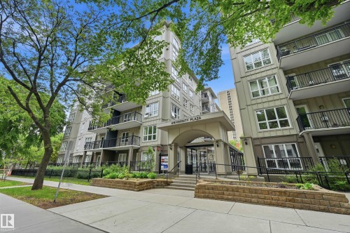 Modern multi-story building featuring a prominent arched entrance with glass doors, multiple private balconies with black railings, and a concrete ramp for accessibility - #203 11103 84 Av Nw, Edmonton, AB - Outdoor With Balcony With Facade