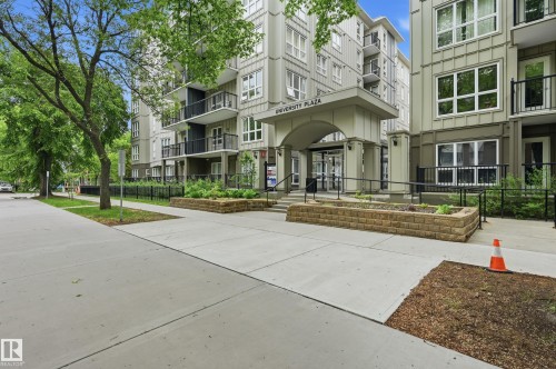 Contemporary multi-story building featuring a prominent arched entry, multiple private balconies with black railings, and a ground-level planted stone retaining wall - #203 11103 84 Av Nw, Edmonton, AB - Outdoor With Balcony With Facade