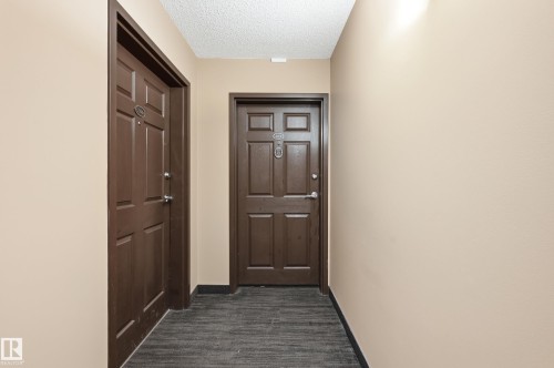 Hallway featuring two paneled entry doors, textured beige walls, and dark flooring - #203 11103 84 Av Nw, Edmonton, AB - Indoor Photo Showing Other Room