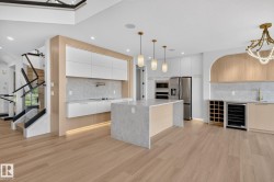 Contemporary kitchen featuring a waterfall island with pendant lighting, integrated appliances, and a built-in wine cooler - 