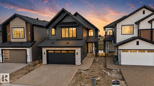 Contemporary exterior featuring dark vertical siding, light stone accents, a black garage door with frosted panels, and a concrete driveway - 8791 Mayday Ln Sw Sw, Edmonton, AB - Outdoor With Facade