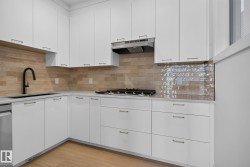Contemporary kitchen featuring white cabinetry, light countertops, wood-finish flooring, a black gooseneck faucet, and a subway tile backsplash - 
