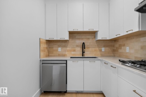 White cabinetry featuring integrated hardware, a stainless steel dishwasher, a black sink with a matte black faucet, and a tiled backsplash - 8791 Mayday Ln Sw Sw, Edmonton, AB - Indoor Photo Showing Kitchen