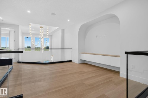 Open concept loft featuring light wood-finish flooring, a contemporary glass railing, and a built-in media console with a wood-finish countertop - 8791 Mayday Ln Sw Sw, Edmonton, AB - Indoor