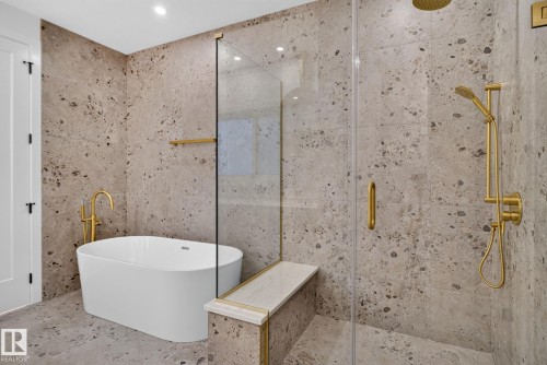 Freestanding soaking tub with a floor-mounted gold-finish faucet, complemented by a spacious walk-in shower featuring gold-finish fixtures, a built-in bench with a stone top, and full-height stone-look tile walls - 8791 Mayday Ln Sw Sw, Edmonton, AB - Indoor Photo Showing Bathroom