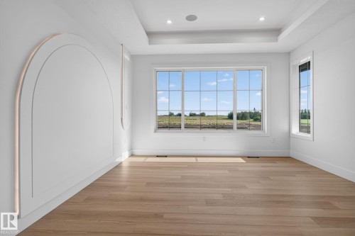 Spacious room featuring multiple windows, wood-finish flooring, recessed ceiling lighting, a tray ceiling, and decorative wall molding with integrated lighting - 8791 Mayday Ln Sw Sw, Edmonton, AB - Indoor Photo Showing Other Room
