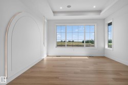 Spacious room featuring multiple windows, wood-finish flooring, recessed ceiling lighting, a tray ceiling, and decorative wall molding with integrated lighting - 