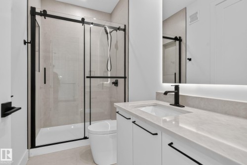 Contemporary bathroom featuring a frameless glass shower enclosure with matte black hardware, a pristine white toilet, a floating vanity with a light-toned countertop and integrated sink, a matte black faucet, and an illuminated mirror - 8791 Mayday Ln Sw Sw, Edmonton, AB - Indoor Photo Showing Bathroom