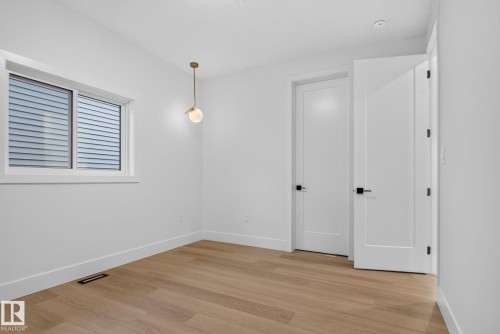 Bright, open bedroom featuring warm wood-finish flooring, white painted walls, and abundant natural light from a large multi-pane window - 8791 Mayday Ln Sw Sw, Edmonton, AB - Indoor Photo Showing Other Room