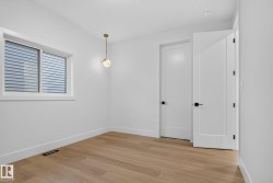 Bright, open bedroom featuring warm wood-finish flooring, white painted walls, and abundant natural light from a large multi-pane window - 