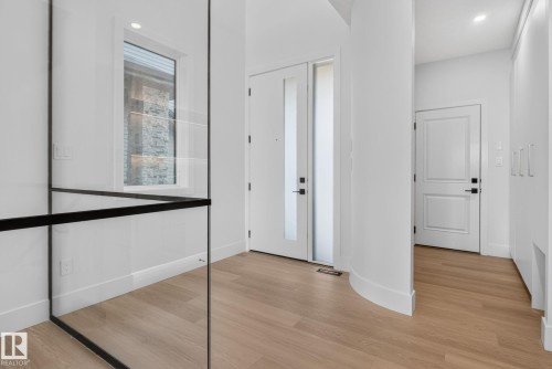 Entryway featuring light wood-finish flooring, a contemporary glass and black metal railing, and a window with stone exterior elements - 8791 Mayday Ln Sw Sw, Edmonton, AB - Indoor Photo Showing Other Room