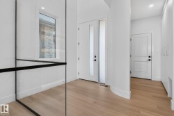 Entryway featuring light wood-finish flooring, a contemporary glass and black metal railing, and a window with stone exterior elements - 