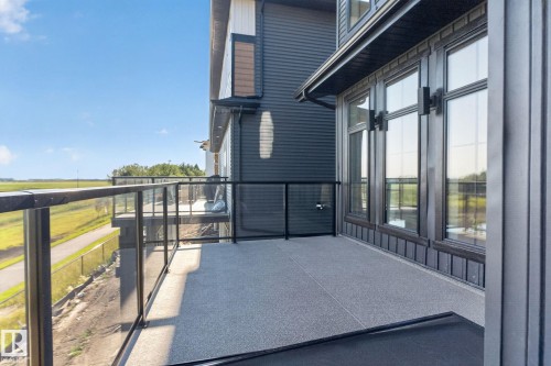 Elevated balcony featuring a glass railing system, textured grey flooring, dark siding, and large windows with black trim - 8791 Mayday Ln Sw Sw, Edmonton, AB - Outdoor With Exterior
