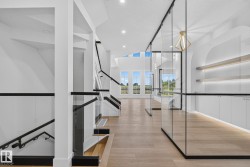 Modern interior featuring light wood-finish flooring and a contemporary staircase with glass railings and dark banisters - 