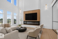 Two-story living area featuring a wood-panelled media wall with an integrated linear fireplace, large windows providing abundant light, wood-finish flooring, and contemporary wall sconces - 