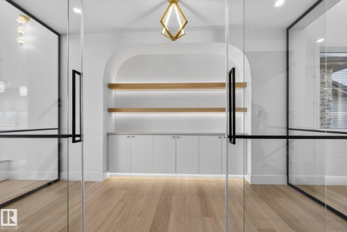 Glass-enclosed room featuring a custom arched built-in with two light wood-finish floating shelves, under-cabinet lighting, and white cabinetry - 8791 Mayday Ln Sw Sw, Edmonton, AB - Indoor