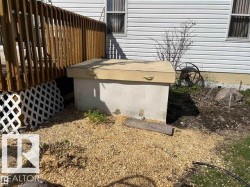 Concrete utility access with a top-mounted handle, situated alongside a wood deck with lattice skirting and white vinyl siding - 