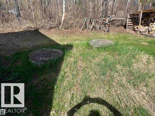 Grassy outdoor area featuring two circular concrete covers, a wood storage structure, and surrounding natural foliage - 210 55504 Nikoodi Road, Rural Lac Ste. Anne County, AB - Outdoor