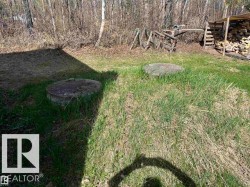 Grassy outdoor area featuring two circular concrete covers, a wood storage structure, and surrounding natural foliage - 