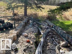 Gravel pathway bordered by wood stumps and natural wood elements, with a mature evergreen tree providing natural shade - 