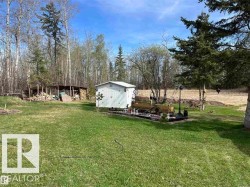 Spacious backyard featuring a manicured lawn, white storage shed, and a rustic wood storage structure - 