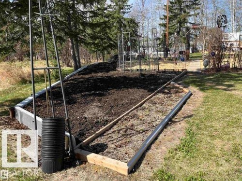 Raised garden bed with dark soil, bordered by wood and concrete, featuring a metal trellis - 210 55504 Nikoodi Road, Rural Lac Ste. Anne County, AB - Outdoor
