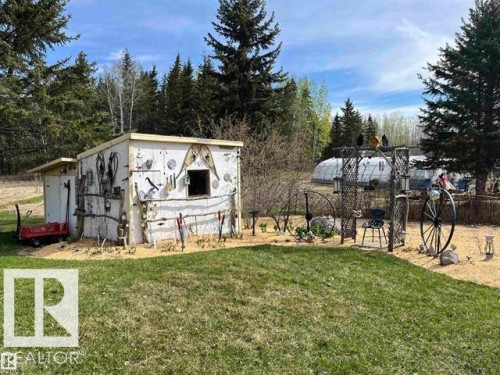 Landscaped outdoor area featuring a decorative shed, mature trees, and a visible greenhouse structure - 210 55504 Nikoodi Road, Rural Lac Ste. Anne County, AB - Outdoor