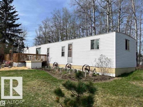 White siding exterior with a wood deck, mature trees, and a garden area - 210 55504 Nikoodi Road, Rural Lac Ste. Anne County, AB - Outdoor