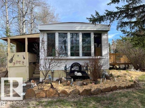 White siding exterior with multiple large windows, a covered entrance, and a wood deck - 210 55504 Nikoodi Road, Rural Lac Ste. Anne County, AB - Outdoor