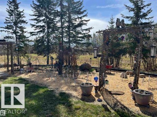 Expansive yard featuring mature evergreen trees, a decorative arbor, and defined garden beds - 210 55504 Nikoodi Road, Rural Lac Ste. Anne County, AB - Outdoor With View