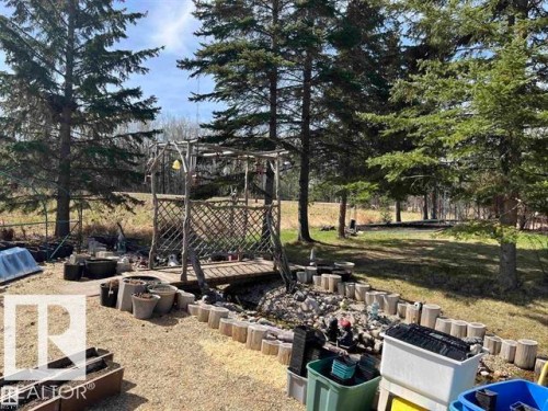 Outdoor space featuring a decorative wooden bridge over a small rock-lined channel, surrounded by mature coniferous trees - 210 55504 Nikoodi Road, Rural Lac Ste. Anne County, AB - Outdoor