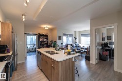 Open-concept living space featuring a kitchen island with dual sinks, light wood-finish flooring, recessed lighting, and a kitchen with stainless steel appliances - 